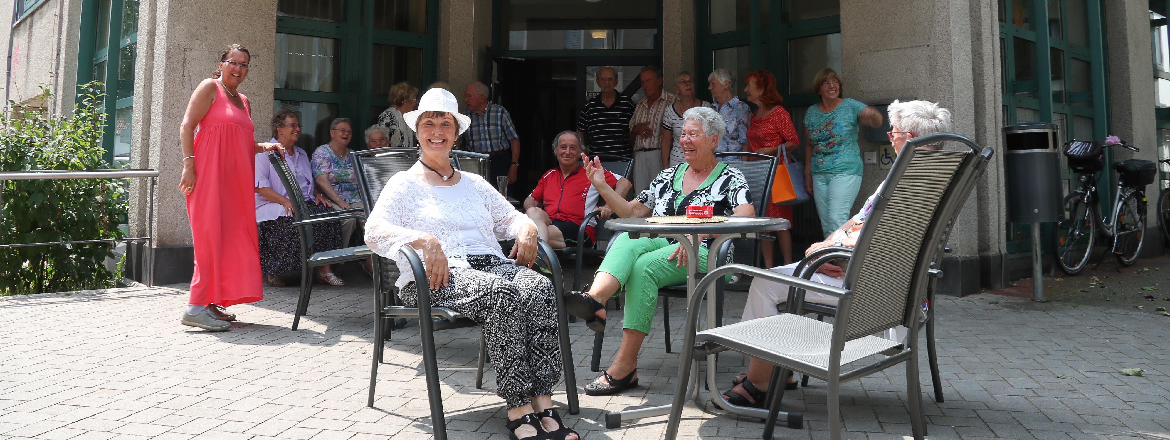 Vor dem Gebäude des Seniorentreffs sitzen Besucher in der Sonne.