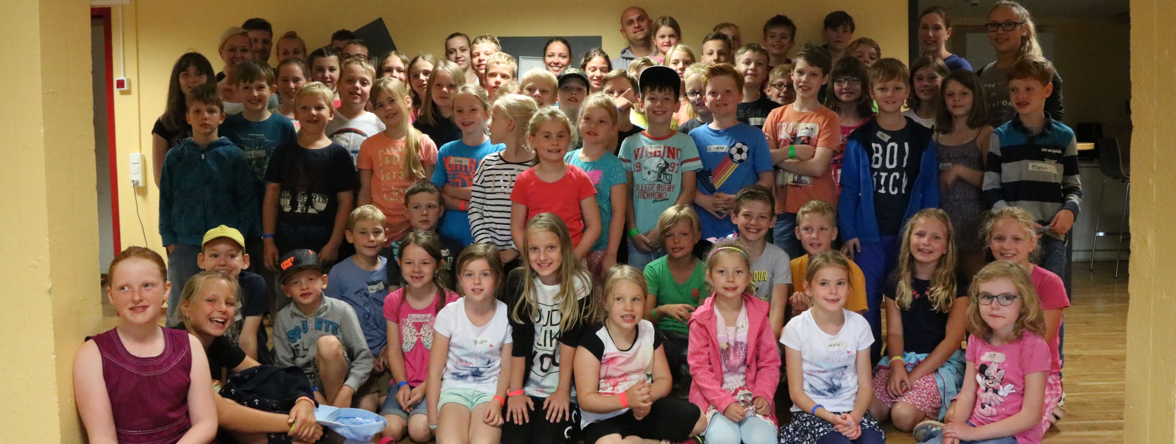 60 Kinder und 12 Betreuer haben sich zum Gruppenfoto aufgestellt. Einige der Kinder sitzen in der ersten Reihe.