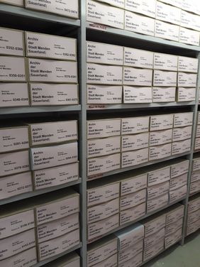 Regale gefüllt mit Kartons voller Akten aus dem Stadtarchiv. Die Kartons sind genaustens beschriftet, damit nichts durcheinander kommt oder verloren geht.