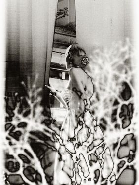 Zu sehen ist eine Frau im Brautkleid, die aus dem Fenster schaut. Der Vordergrund des Bildes ist verzerrt