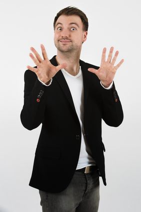 Der Zauberkünstler Christopher Köhler macht eine typische Handbewegung, indem er die Hände vor sich hält, mit den Handflächen zum Publikum und auseinander gespreizten Fingern.