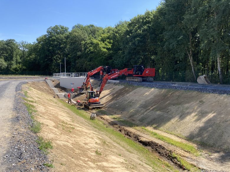 Paralleler Einsatz zweier Bagger am Regenrückhaltebecken 2.2. Der vordere unterstützt die Arbeiter beim Setzen der Betonhalbschalen für die Abflussrinne, der hintere setzt die Pallisaden am Ablauf, die zur Rückhaltung mitgeführter Schwimmstoffe wie Äste, Laub etc. dienen.