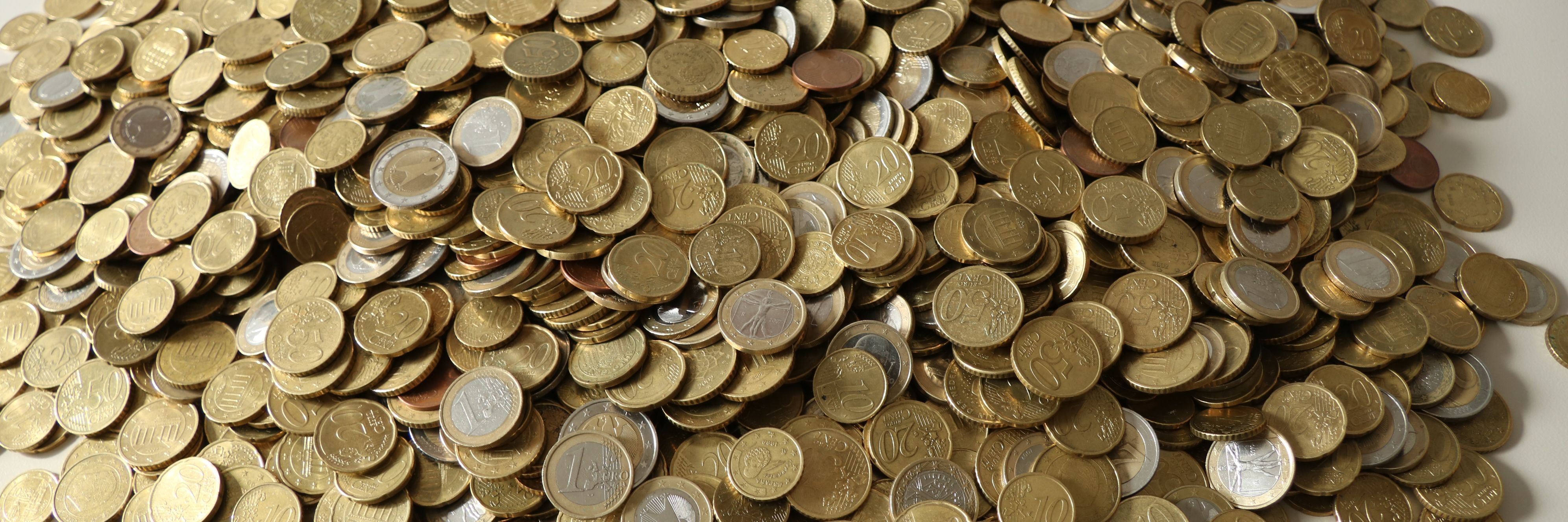 Auf einem weißen Tisch liegen zahllose Euro-Münzen auf einem großen Haufen.