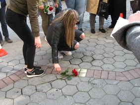 Auf dem Foto ist eine der verantwortlichen Schülerinnen zu sehen, die das Projekt mit ins Rollen gebracht hat. Sie legt eine Rose auf die Stolpersteine während der Eröffnung nieder. 