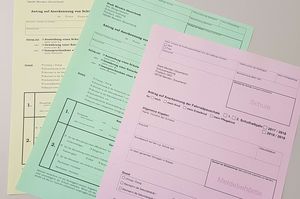Das Bild zeigt drei Anträge auf gelbem, grünem und rosa farbigem Papier.