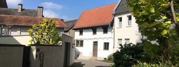 Blick auf das Schmarotzerhaus. Im Vordergrund stehen rechts ein Baum und links einige Sträucher, die das Schmarotzerhaus einrahmen.