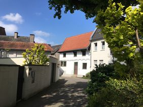 Blick auf das Schmarotzerhaus. Im Vordergrund stehen rechts ein Baum und links einige Sträucher, die das Schmarotzerhaus einrahmen.