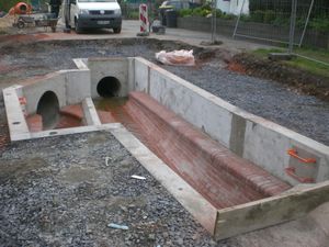 Neubau des Regenüberlaufes "Alte Kläranlage", in Fließrichtung gesehen. Das Bauwerk ist außen mit Stahlbeton errichtet, innen geklinkert. Die Abdeckung ist noch nicht montiert, so dass ein Einblick in das Gerinne möglich ist. Hinten rechts der Ablauf, hier wird später noch eine Drosseleinrichtung zur Abflussreduzierung eingebaut. Links erfolgt bei Regenwetter der Abfluss des Regenwassers (der sog. "Abschlag") über eine Betonschwelle in Richtung Hönne.