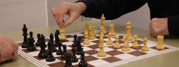 Ein Schachbrett an dem zwei ältere Herren sitzen und spielen