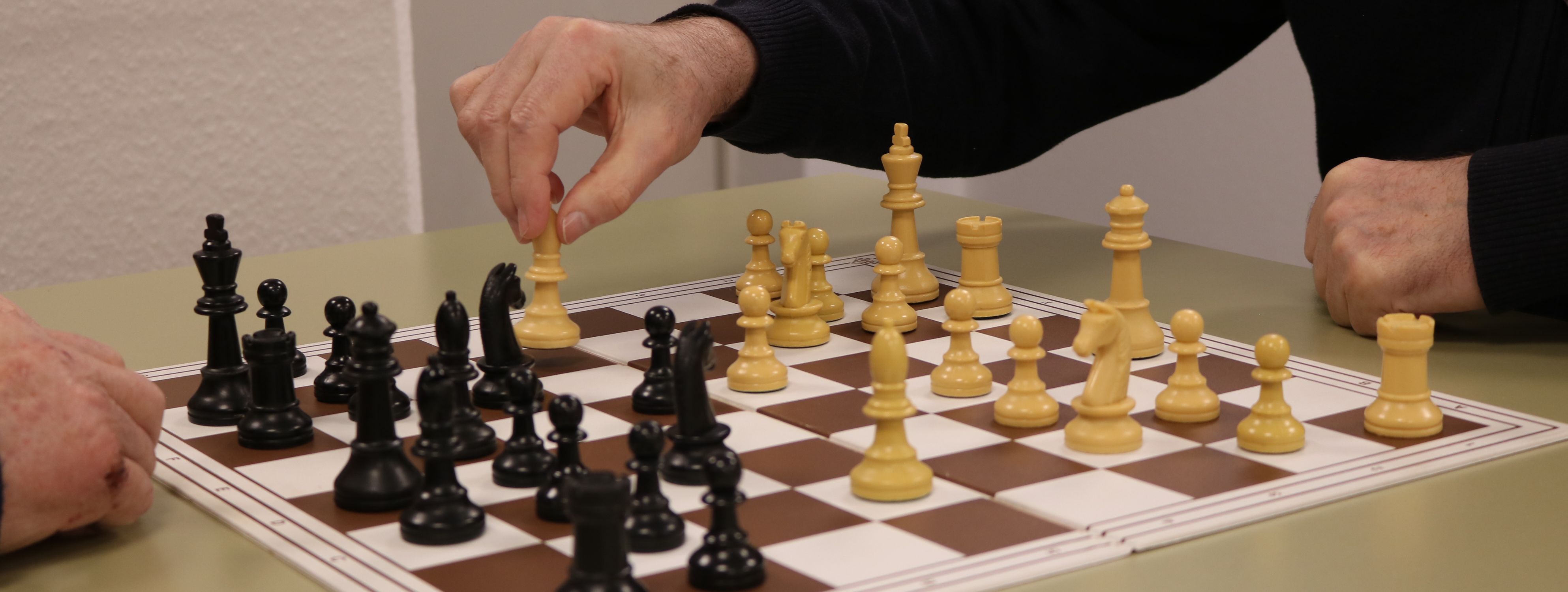 Ein Schachbrett an dem zwei ältere Herren sitzen und spielen