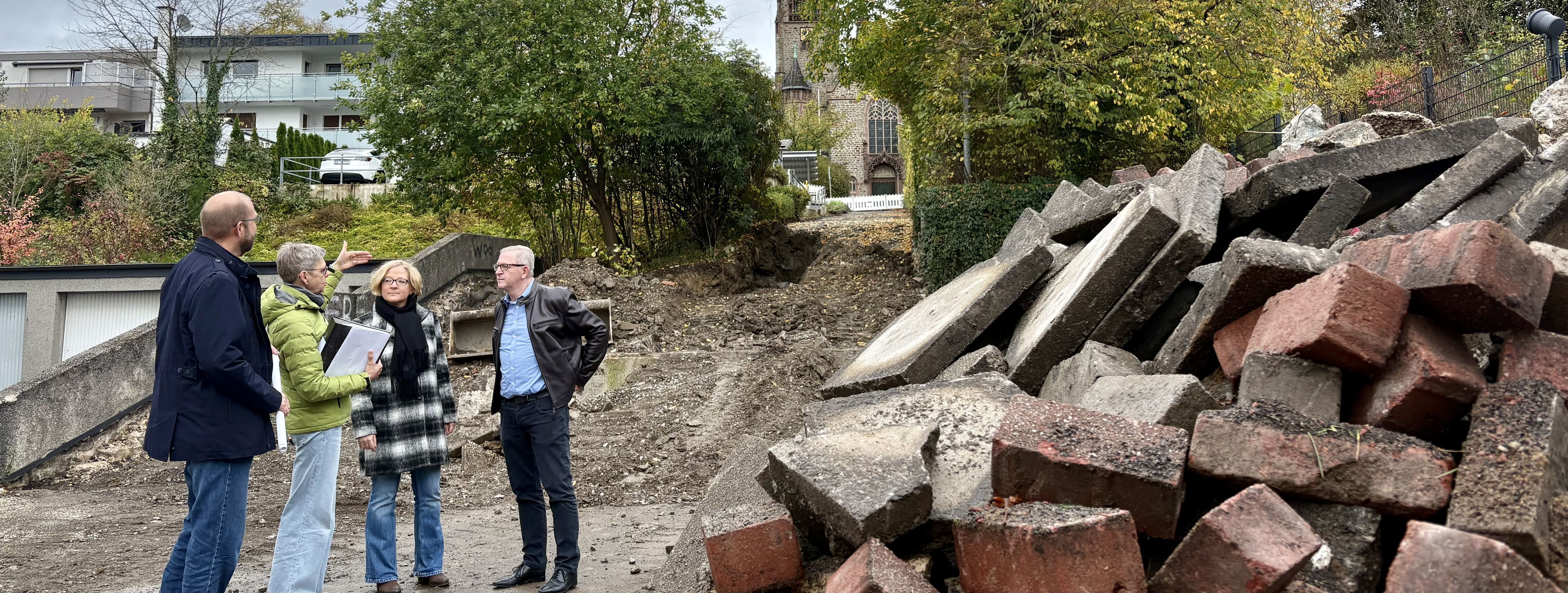 Baudezernent Tobias Wilms und Dagmar Gerling, Teamleiterin Bauen der Abteilung Straßenbau und Verkehr, zeigen Bürgermeister Dr. Roland Schröder und Manuela Schmidt die Pläne der jetzt beginnenden Baumaßnahme der Lebensader Lendringsen Mitte sowie die ersten Arbeiten am Treppenaufgangs zur Kir-che St. Josef.