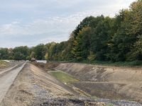 Aushub für das Regenrückhaltebecken 2.2. Vorne rechts befindet sich eine Rampe, über die man für Unterhaltungsarbeiten (Mäharbeiten etc.) in das Becken fahren kann. Die grauen Schächte im Hintergrund sind die Drosselbauwerke.