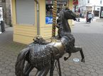 Zu sehen ist das Kirmesdenkmal in Menden beim Alten Rathaus. Es handelt sich um ein Karusselpferd aus Bronze. Das Foto zeigt das Pferd hinten-seitlich.