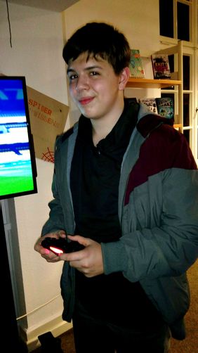 Conrad Brinkmann, Gaming-Experte der Stadtbücherei Menden, hält einen Controler für ein Videospiel in Händen und lächelt verschmitzt in die Kamera