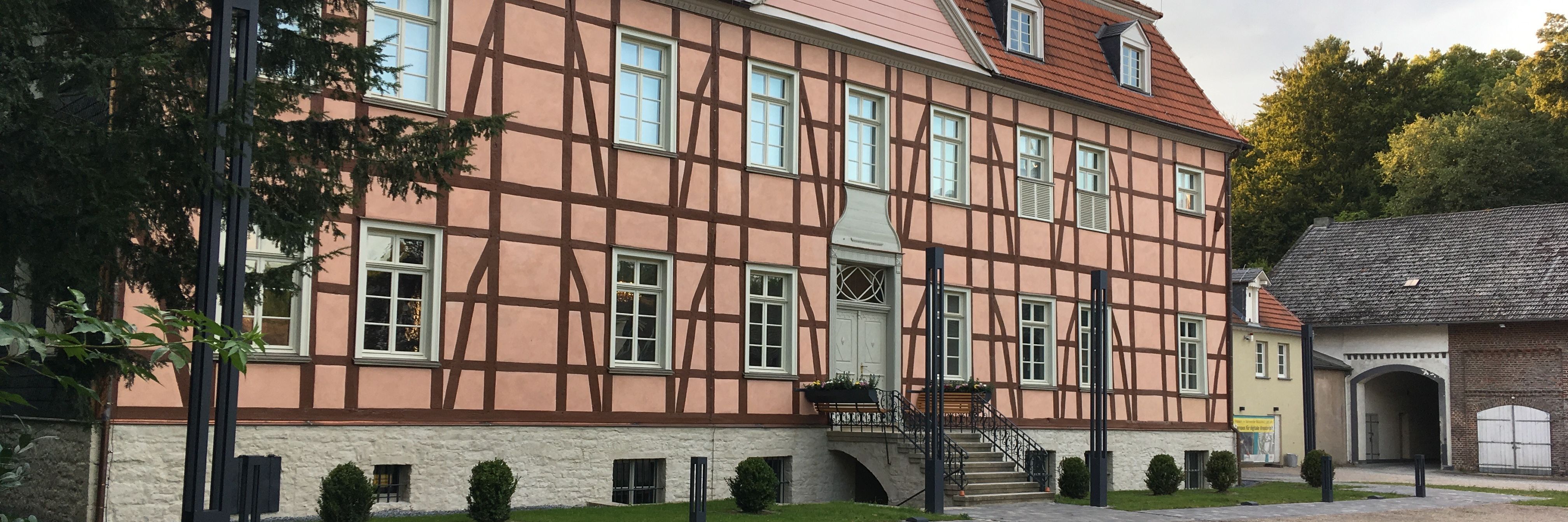 Das rosa verputzte Herrenhaus, seitlich fotografiert, mit grünem Gebüsch am linken Bildrand