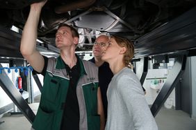 DEKRA Prüfingenieur Oliver Nölle, Bürgermeister Martin Wächter und der erste Kunde des SafetyCheck Nils Flor, stehen gemeinsam unter einem Auto, das auf einer Hebebühne steht.