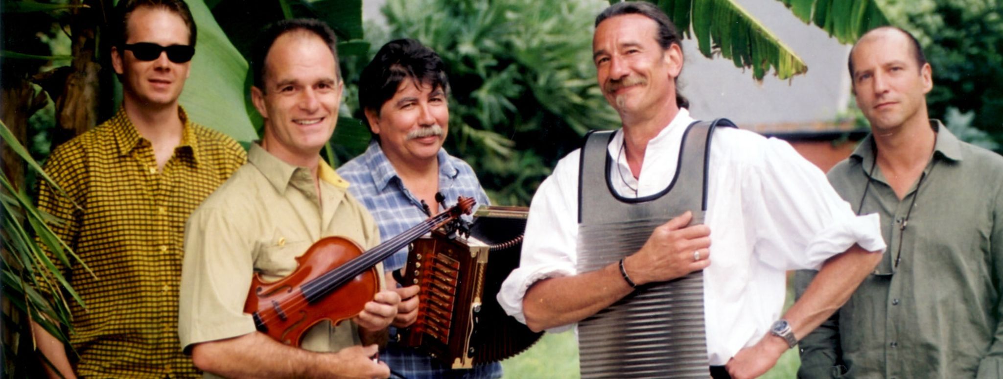 Die fünf Musiker von Le Clou stehen vor einem karibischen Hintergrund mit Palmen, einer hält eine Geige im Arm, ein anderer ein Akkordeon, ein dritter hat sich ein waschbrettartiges Instrumment um den Hals gehängt