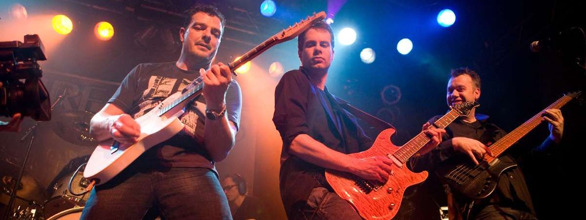 drei Musiker mit E-Gitarren stehen auf der Bühne