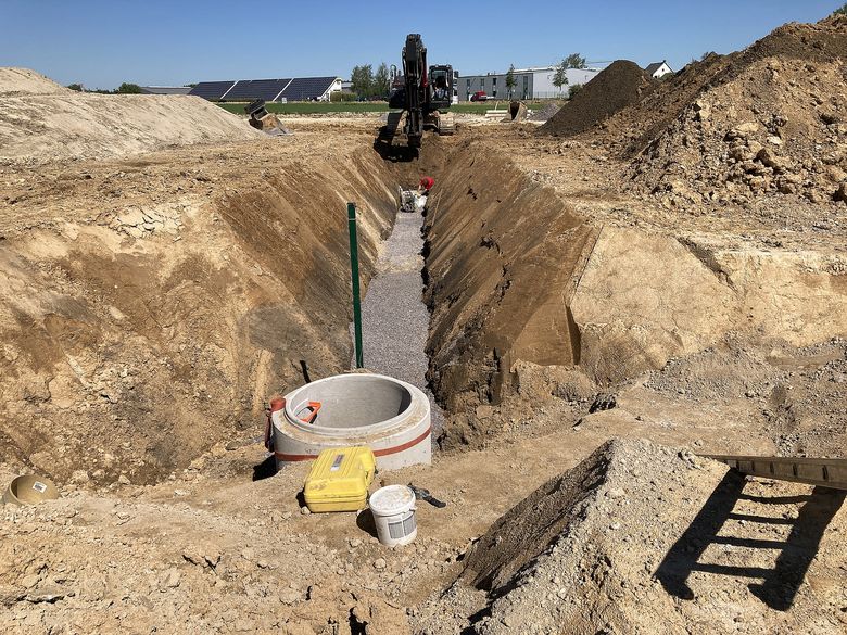 Im Mai / Juni 2021 wurden bereits die ersten Schmutzwasserkanäle im Bereich der künftigen Erschließungsstraße verlegt. Das Bild zeigt den bereits mit Kies verfüllten Leitungsbereich und den geböschten Rohrgraben.