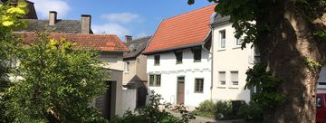 Blick auf das Schmarotzerhaus. Im Vordergrund stehen rechts ein Baum und links einige Sträucher, die das Schmarotzerhaus einrahmen.