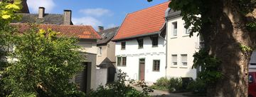 Blick auf das Schmarotzerhaus. Im Vordergrund stehen rechts ein Baum und links einige Sträucher, die das Schmarotzerhaus einrahmen.