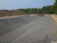 Fertig ausgehobenes Regenrückhaltebecken im Gewerbegebiet Hämmer-Nord, Mai 2011. Die Böschungen des Erdbeckens sind hergestellt und mit Folien abgedeckt. Für eines der künftigen Gewerbegrundstücke wurde bereits ein Anschlussrohr verlegt, das noch in das Becken hineinragt. Dieses Rohr wird später bündig direkt an der Böschungskante enden (Foto: Stadtentwässerung).