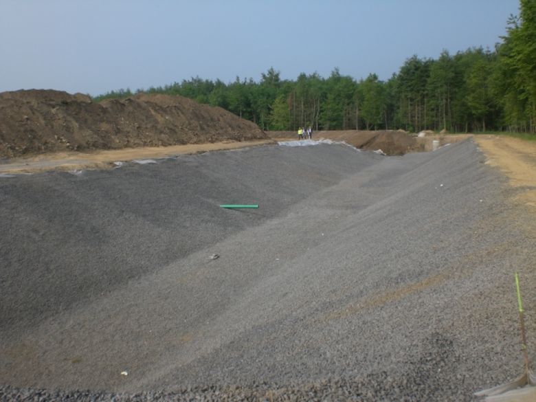 Fertig ausgehobenes Regenrückhaltebecken im Gewerbegebiet Hämmer-Nord, Mai 2011. Die Böschungen des Erdbeckens sind hergestellt und mit Folien abgedeckt. Für eines der künftigen Gewerbegrundstücke wurde bereits ein Anschlussrohr verlegt, das noch in das Becken hineinragt. Dieses Rohr wird später bündig direkt an der Böschungskante enden (Foto: Stadtentwässerung).