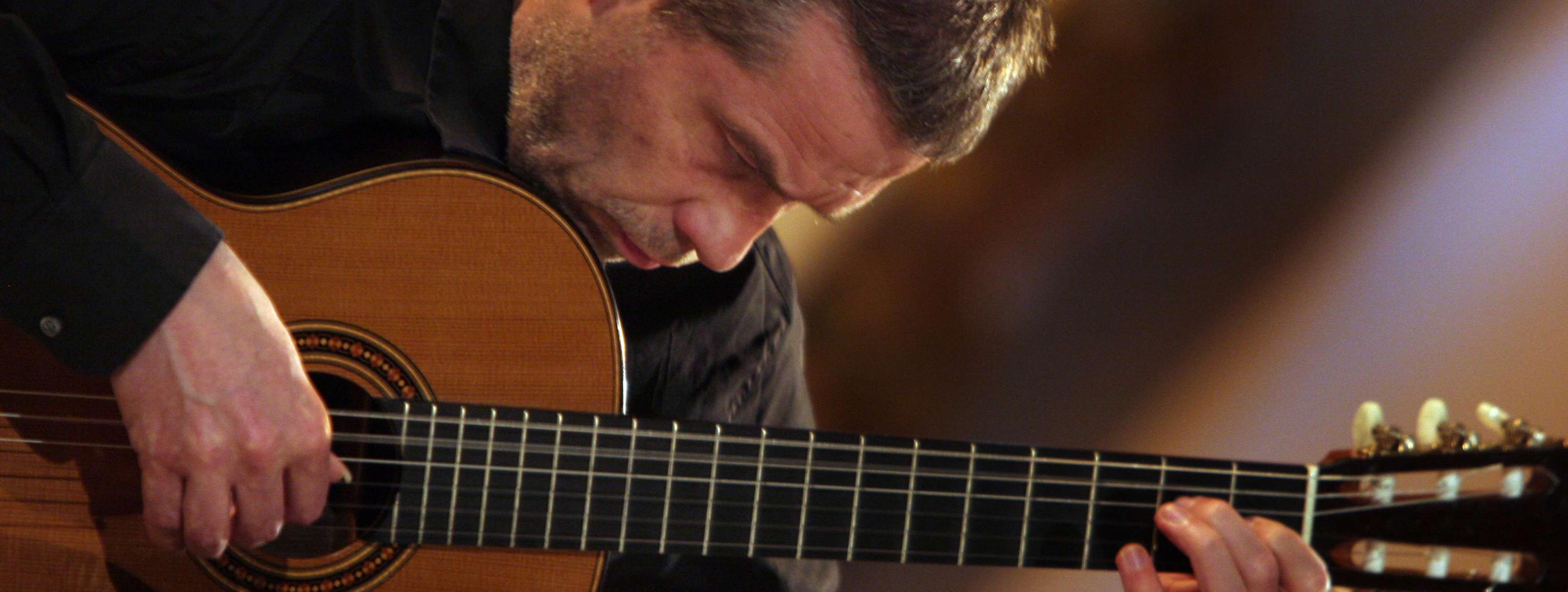 Friedemann Wuttke sitzt dicht geneigt über seine Gitarre und spielt darauf. Er wirkt geradezu vertieft in sein Instrument.