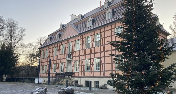 Eine Vorderansicht des rosafarbenen Herrenhauses von Gut Rödinghausen bei frostiger Winterstimmung mit Tannenbaum im Vordergrund.