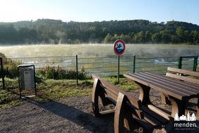 Die neu angelegten Oeseteiche. Auf dem Wasser wabern noch Nebelschwaden. Die Oberfläche der Teiche ist mit allerlei Wasserpflanzen bedeckt. An den abgezäunten Teichen stehen Bänke und ein Tisch, die zum Rasten einladen.