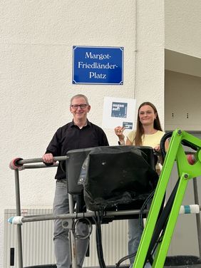 Bürgermeister Dr. Roland Schröder und Ida Zimmermann von Netzwerk „augen auf!“ vor dem Namensschild des neuen Margot-Friedländer-Platzes in Menden.