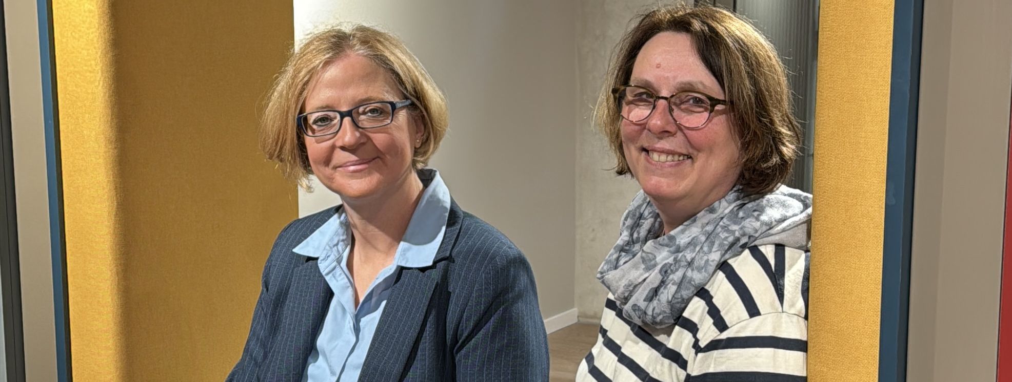 Bürgermeisterin Manuela Schmidt und die stellvertretende Büchereileiterin Sabine Hildebrand sitzen in einer der Sitzecken des neuen Bücherregals