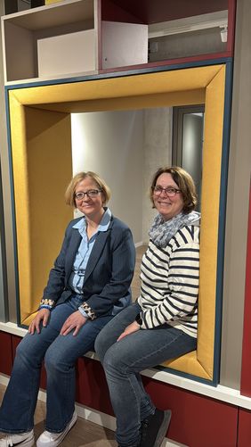 Bürgermeisterin Manuela Schmidt und die stellvertretende Büchereileiterin Sabine Hildebrand sitzen in einer der Sitzecken des neuen Bücherregals