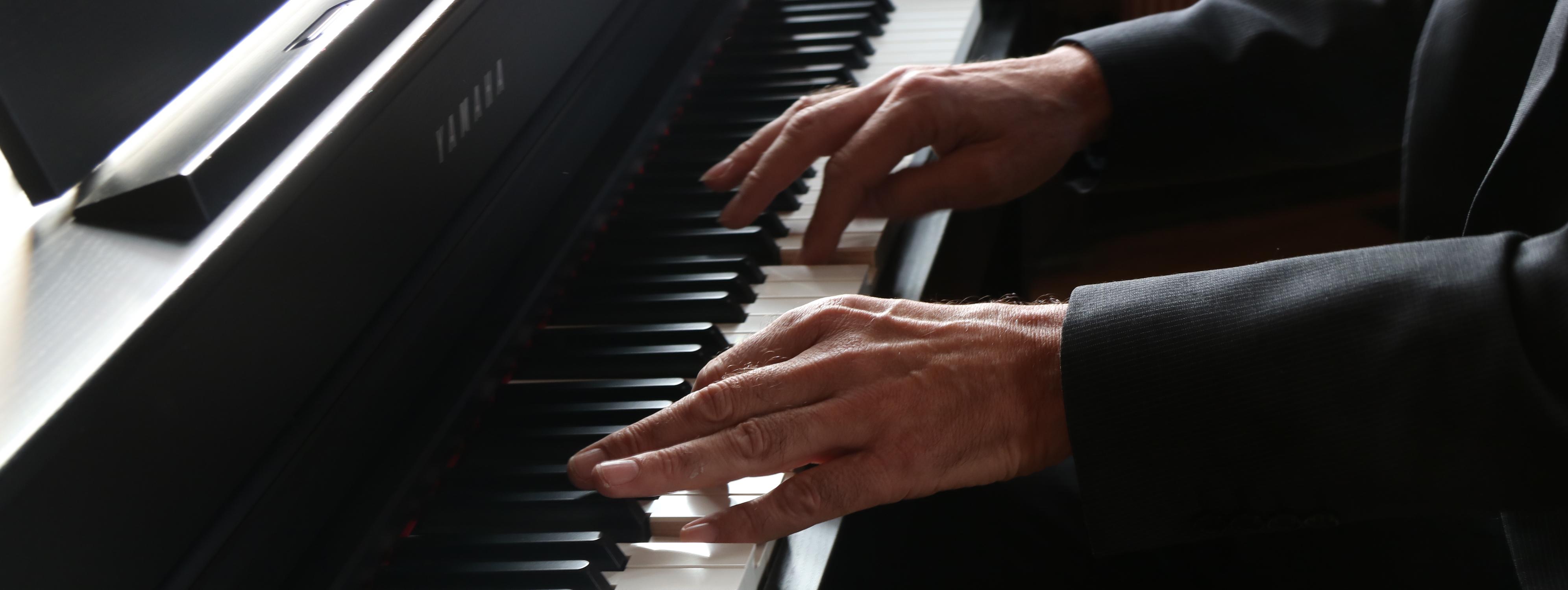 Zu sehen sind die schwarzen und weißen Tasten eines Klaviers und die Hände des Klavierspielers.