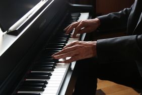 Zu sehen sind die schwarzen und weißen Tasten eines Klaviers und die Hände des Klavierspielers.