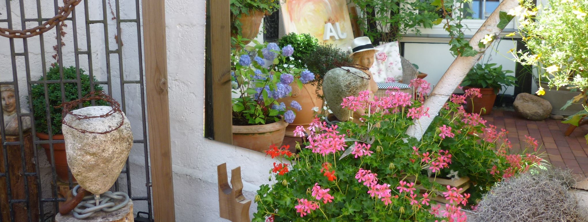 Bunte Blumen stehen in großen Übertöpfen aus Keramik vor einem Fachwerkhaus.