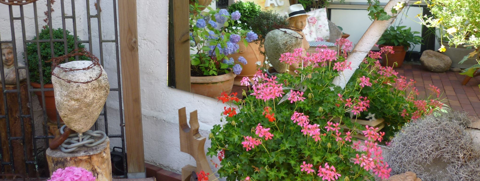 Bunte Blumen stehen in großen Übertöpfen aus Keramik vor einem Fachwerkhaus.