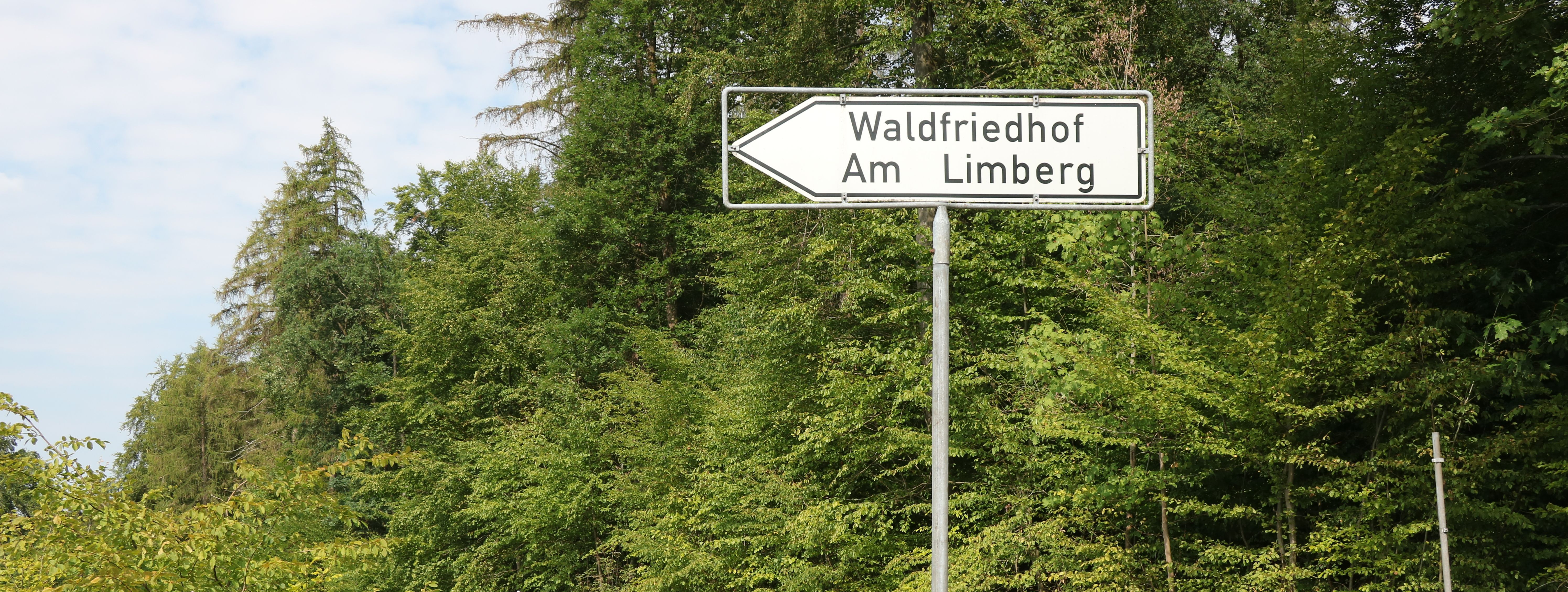 Ein weißes Schild mit schwarzem Text zeigt den Weg zum Friedhal am Limberg