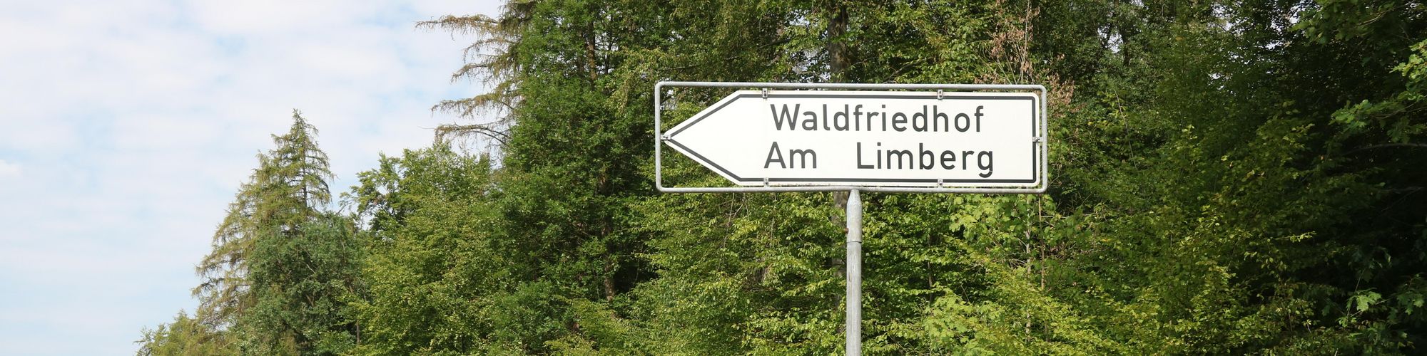 Ein weißes Schild mit schwarzem Text zeigt den Weg zum Friedhal am Limberg