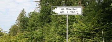 Ein weißes Schild mit schwarzem Text zeigt den Weg zum Friedhal am Limberg