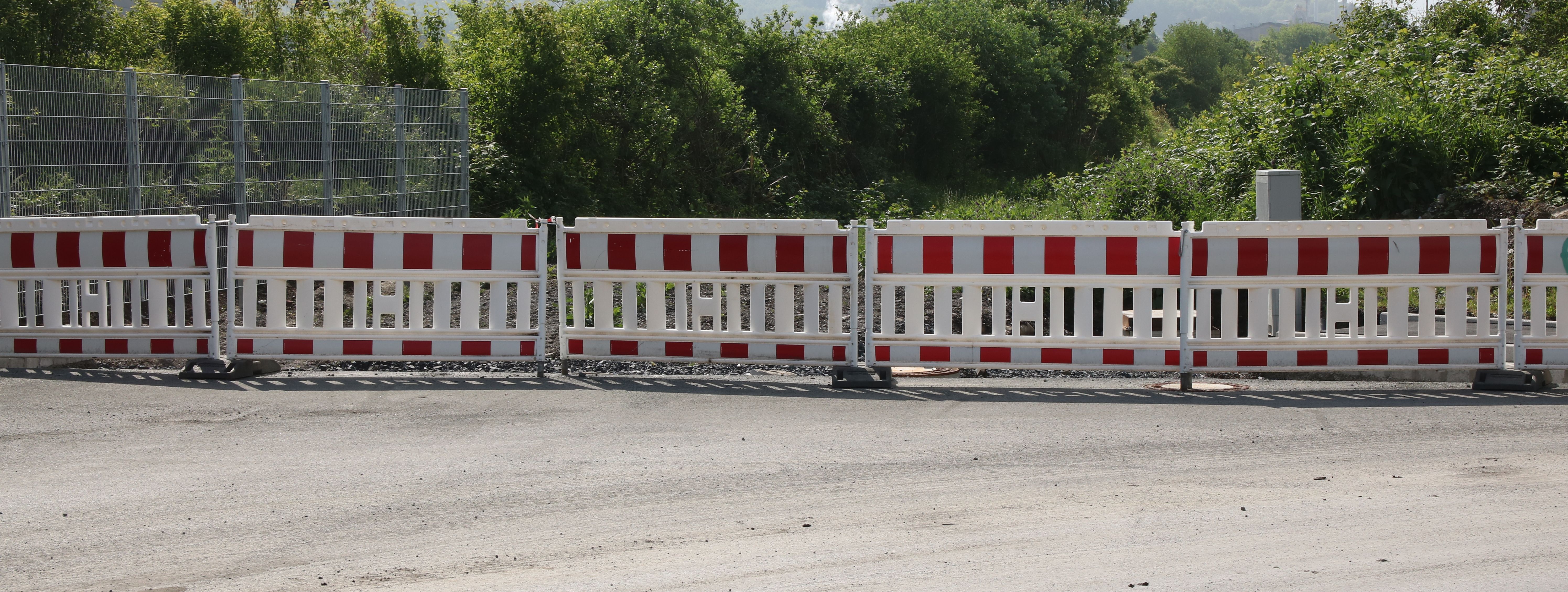 Am Ende einer neugebauten Straße steht eine reihe rot-weißer Baken zur Absperrung.