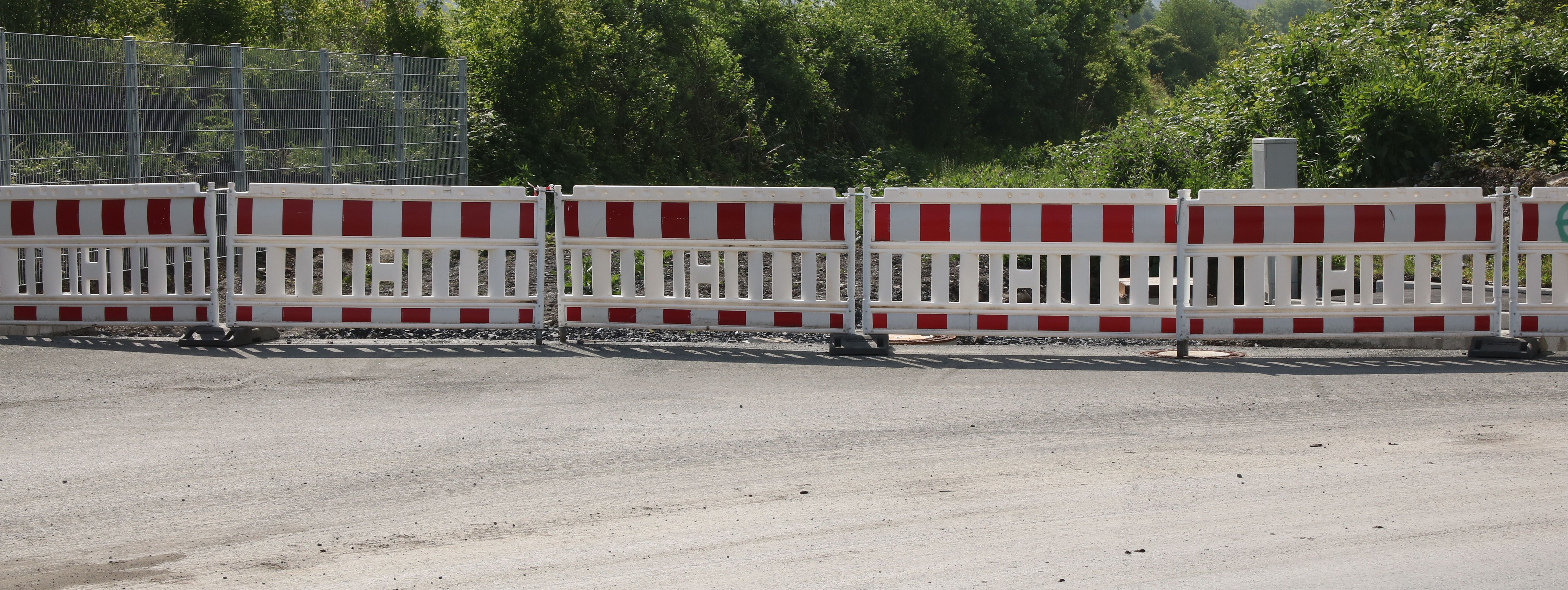 Am Ende einer neugebauten Straße steht eine reihe rot-weißer Baken zur Absperrung.