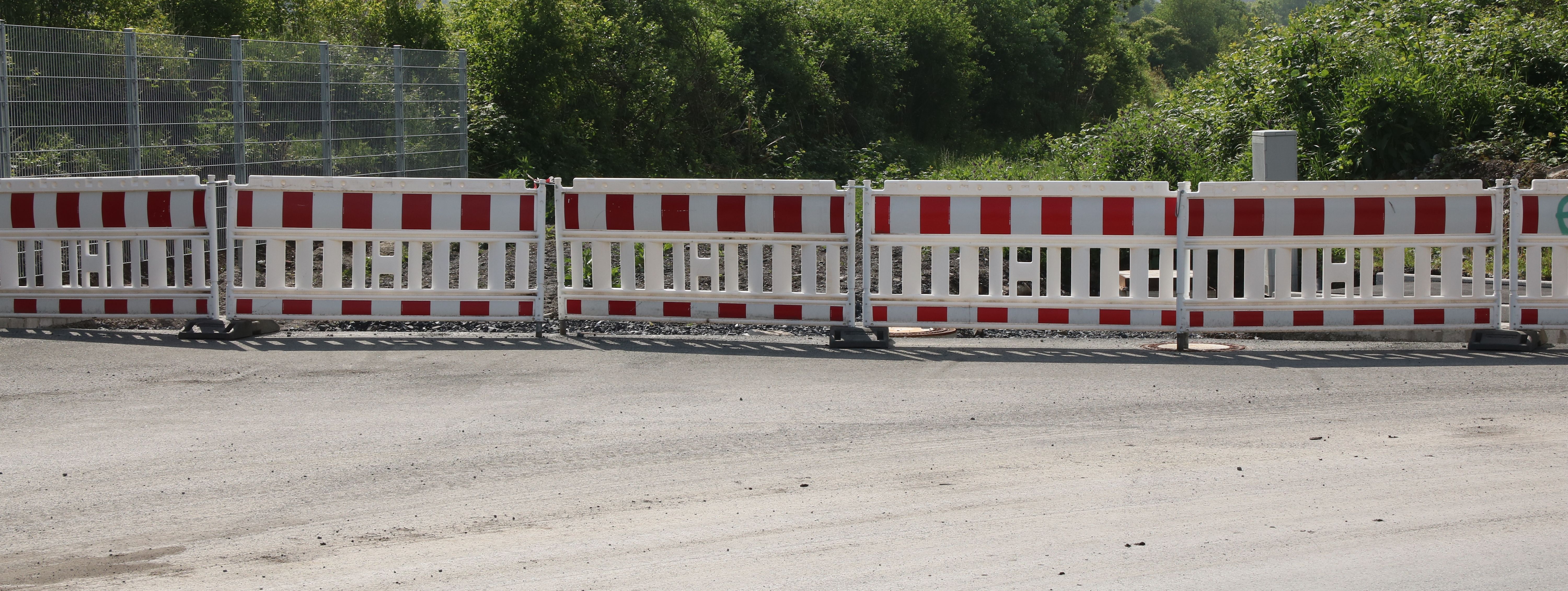 Am Ende einer neugebauten Straße steht eine reihe rot-weißer Baken zur Absperrung.