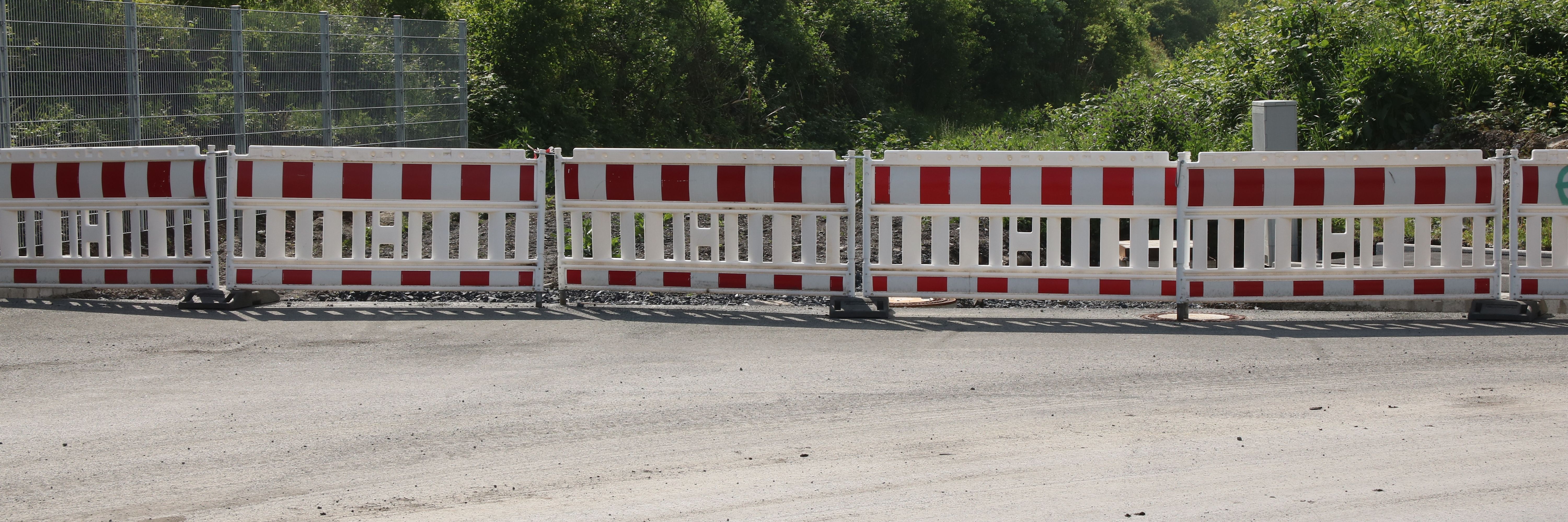 Am Ende einer neugebauten Straße steht eine reihe rot-weißer Baken zur Absperrung.