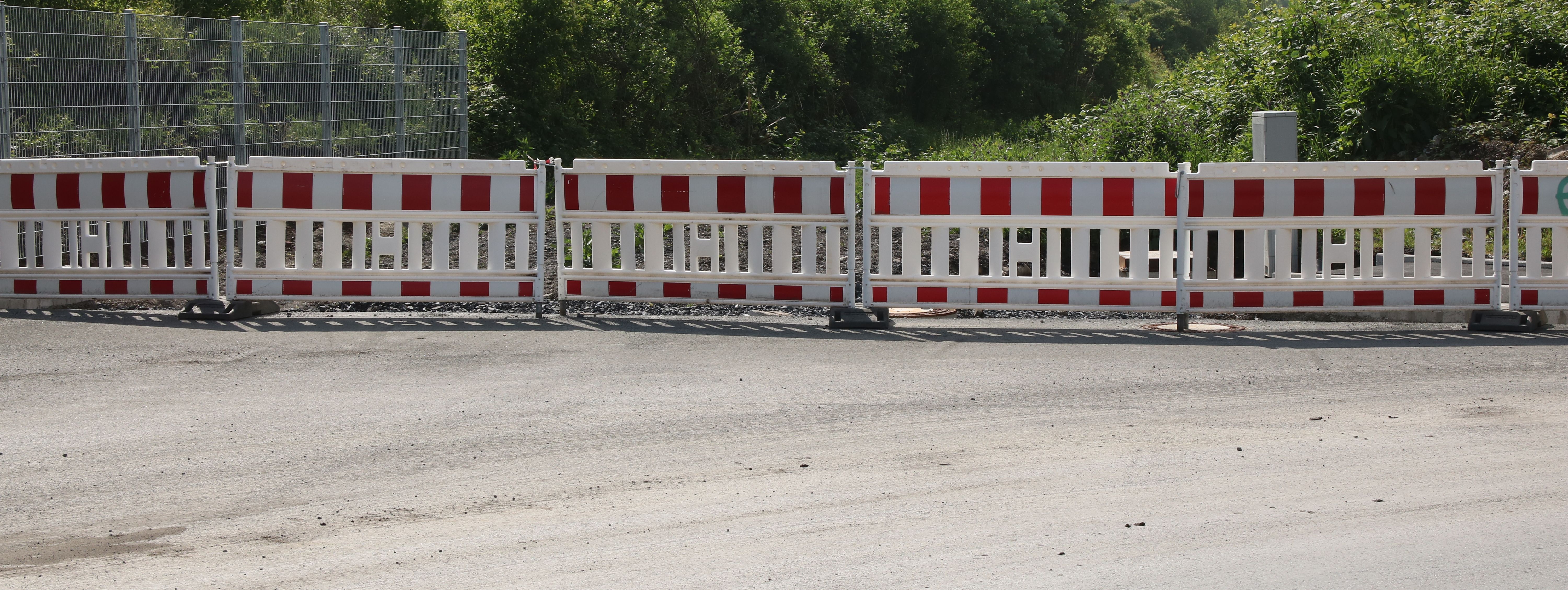 Am Ende einer neugebauten Straße steht eine reihe rot-weißer Baken zur Absperrung.