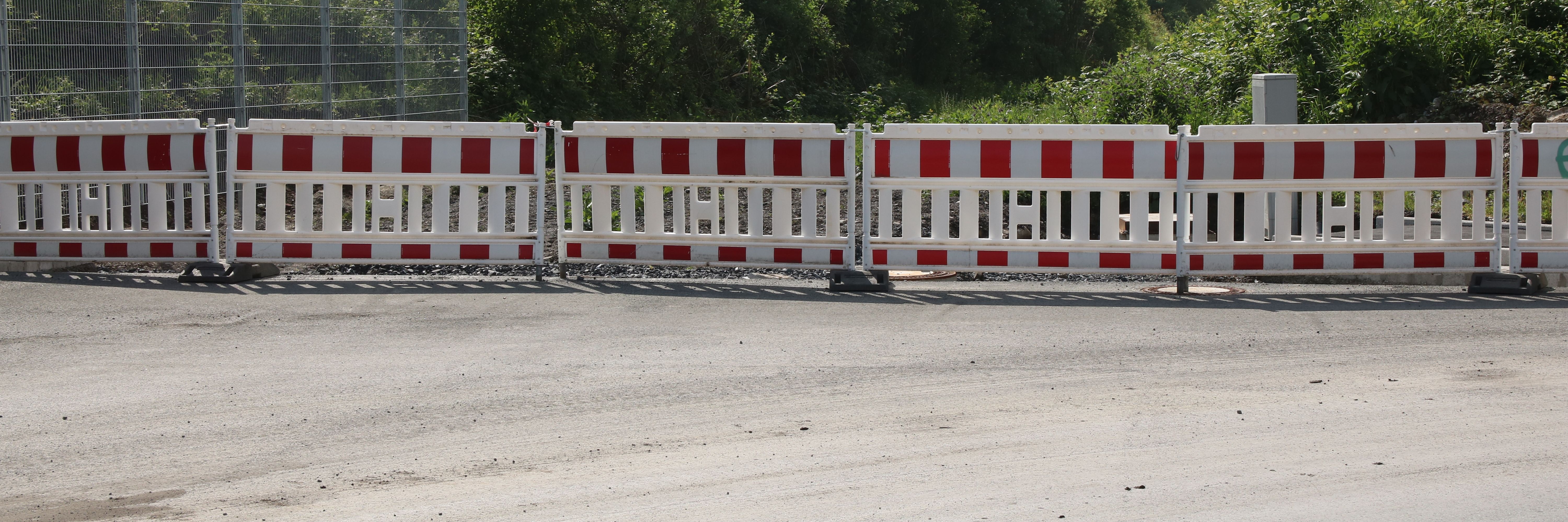 Am Ende einer neugebauten Straße steht eine reihe rot-weißer Baken zur Absperrung.