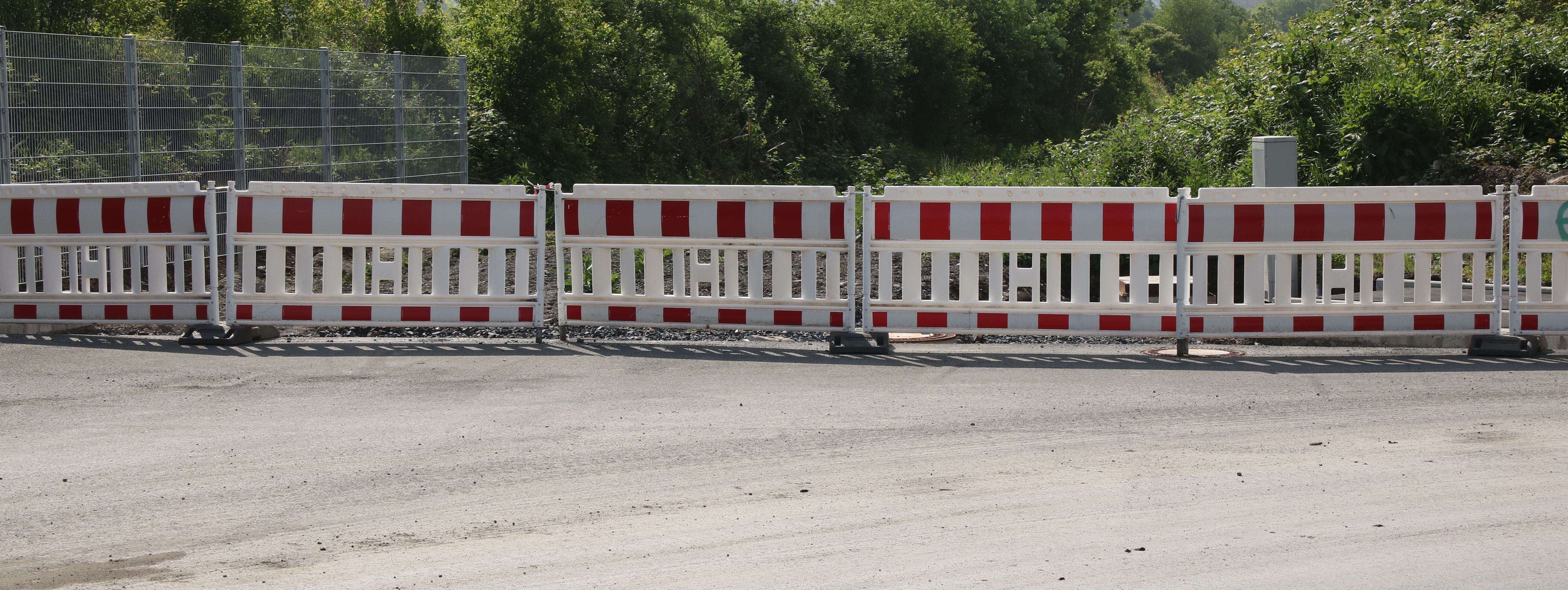 Am Ende einer neugebauten Straße steht eine reihe rot-weißer Baken zur Absperrung.