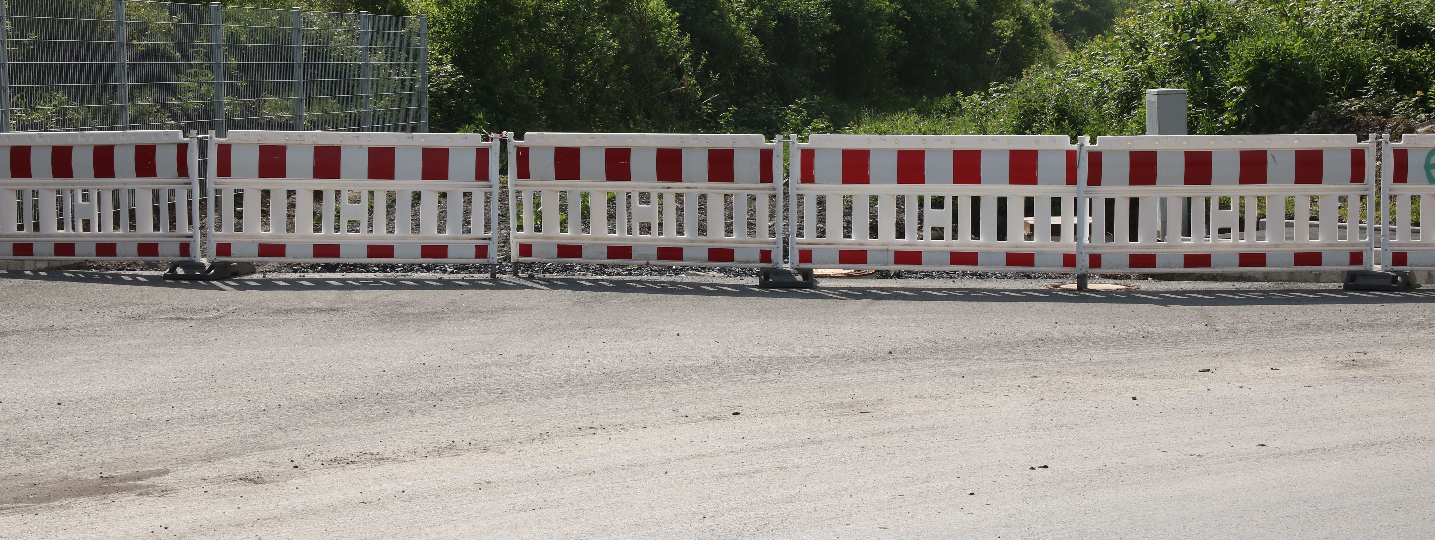 Am Ende einer neugebauten Straße steht eine reihe rot-weißer Baken zur Absperrung.