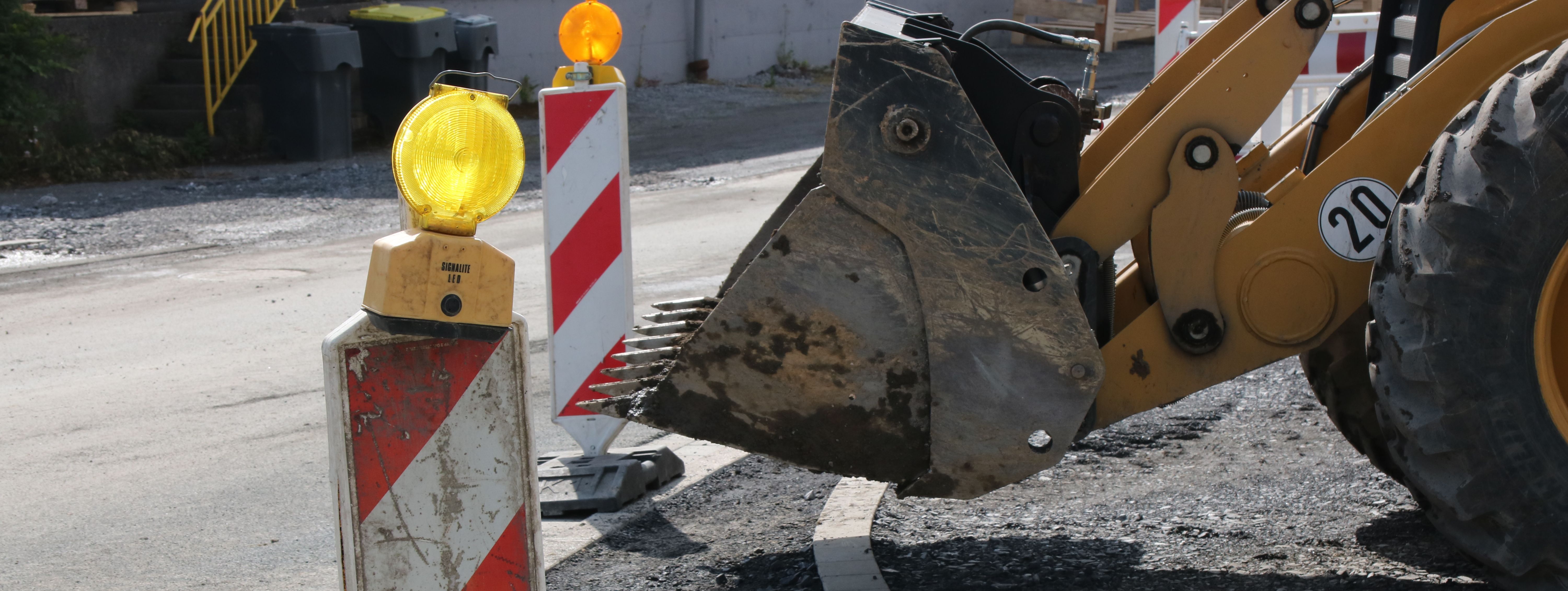 Im Vordergrund steht eine rot-weiße Bake mit gelber Warnleuchte darauf, im Hintergrund sieht man die Schaufel eines Radladers.