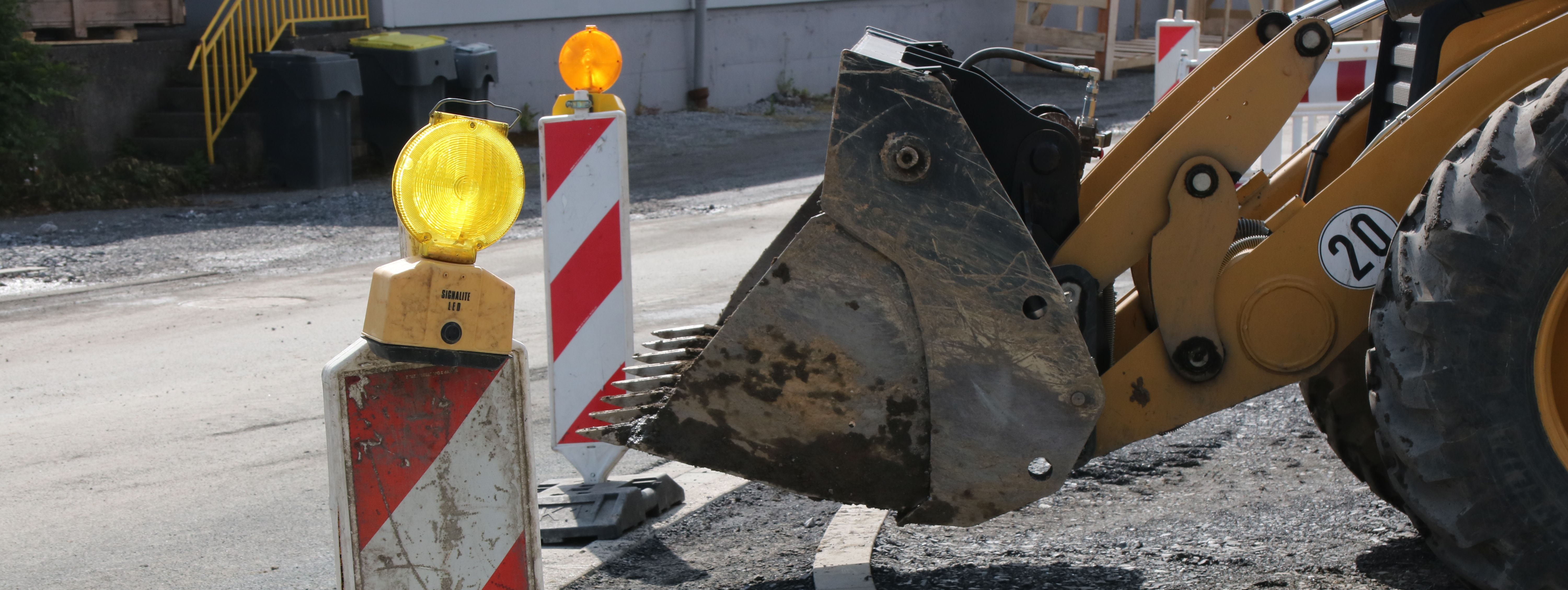 Im Vordergrund steht eine rot-weiße Bake mit gelber Warnleuchte darauf, im Hintergrund sieht man die Schaufel eines Radladers.